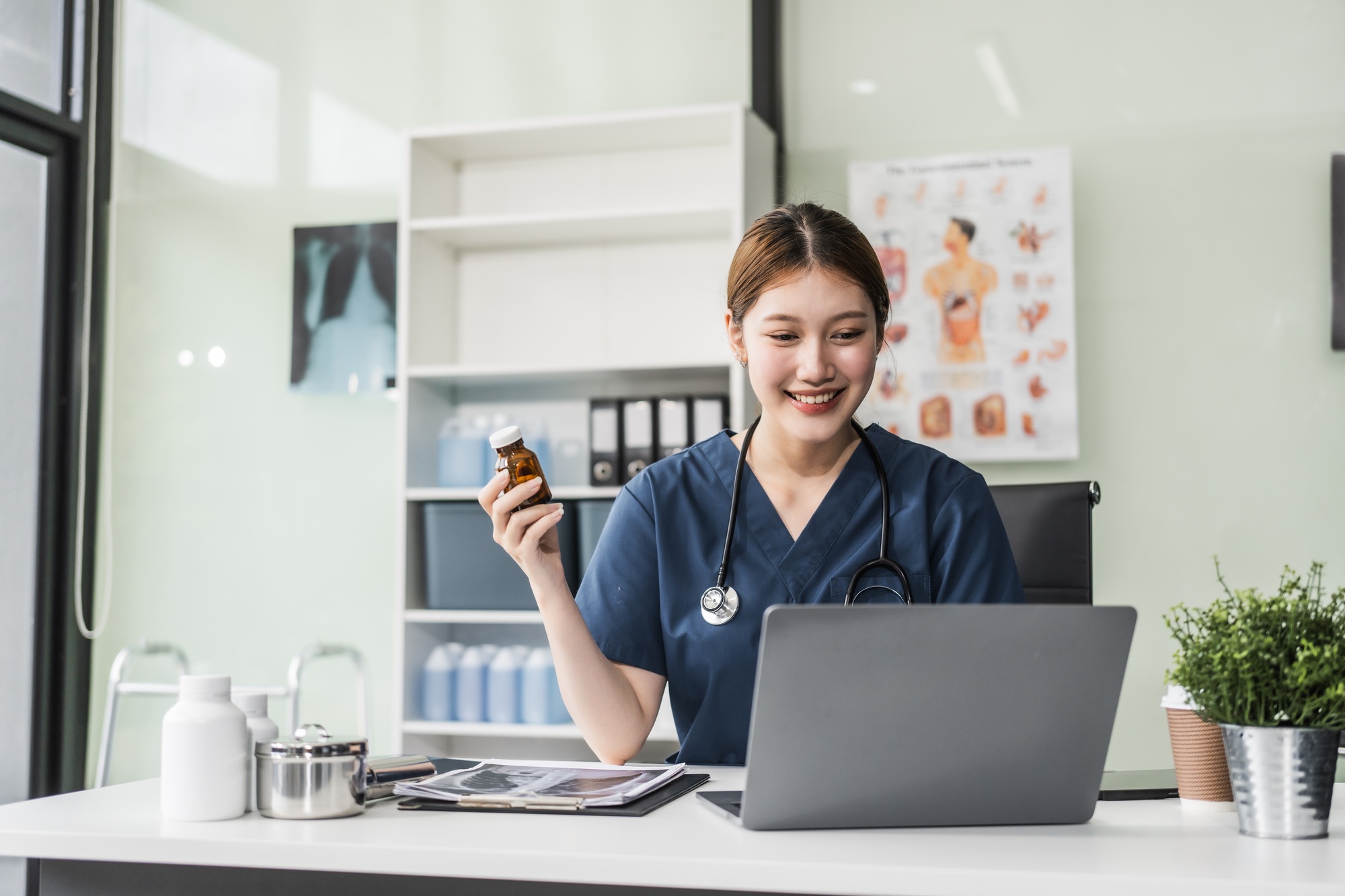 A young Asian nurse providing online consultations, seated at her desk with a laptop. She offers